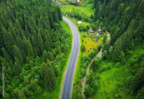 Aerial view of road in beautiful green forest at sunset in summer. Colorful landscape with roadway  pine trees. Carpatian mountains. Top view from drone of highway. View from above. Travel in Ukraine