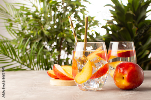 Peach cocktail or lemonade with frsh peaches and tropical plants on background.Close up of refreshing summer cocktail. photo