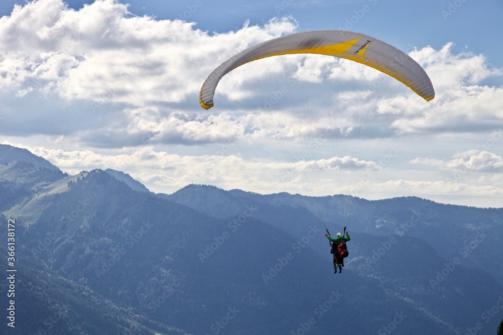Paragliding among the mountains on sunny summer day. Paraglider flight against beautiful mountains landscape and bright sky. Parachuting in the mountains. Human flying high in the sky. Freedom concept Paragliding among the mountains on sunny summer day. Paraglider flight against beautiful mountains landscape and bright sky. Parachuting in the mountains. Human flying high in the sky. Freedom concept