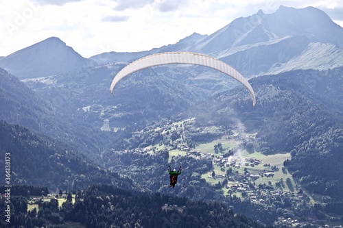 Paragliding among the mountains on sunny summer day. Paraglider flight against beautiful mountains landscape and bright sky. Parachuting in the mountains. Human flying high in the sky. Freedom concept