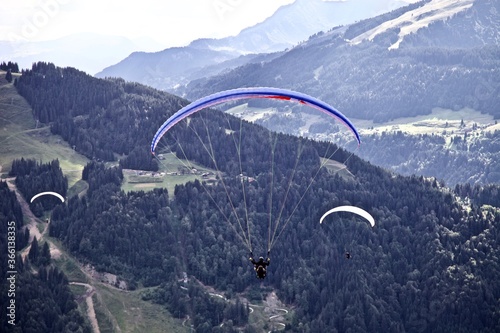 Paragliding among the mountains on sunny summer day. Paraglider flight against beautiful mountains landscape and bright sky. Parachuting in the mountains. Human flying high in the sky. Freedom concept