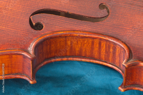 Das F Loch einer Geige mit der Rundung und dem Rand des Korpus. Das Instrument liegt auf einem seidenen blauen Tuch.