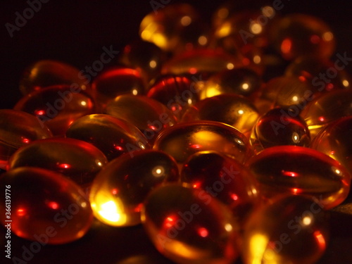 Trans-lucid cod liver oil pills under colourful light © carla