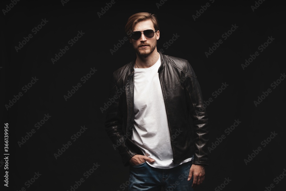 Fashion man, Handsome serious beauty male model portrait wear sunglasses and leather jacket, young guy over black background Fashion man, Handsome serious beauty male model portrait wear sunglasses and leather jacket, young guy over black background