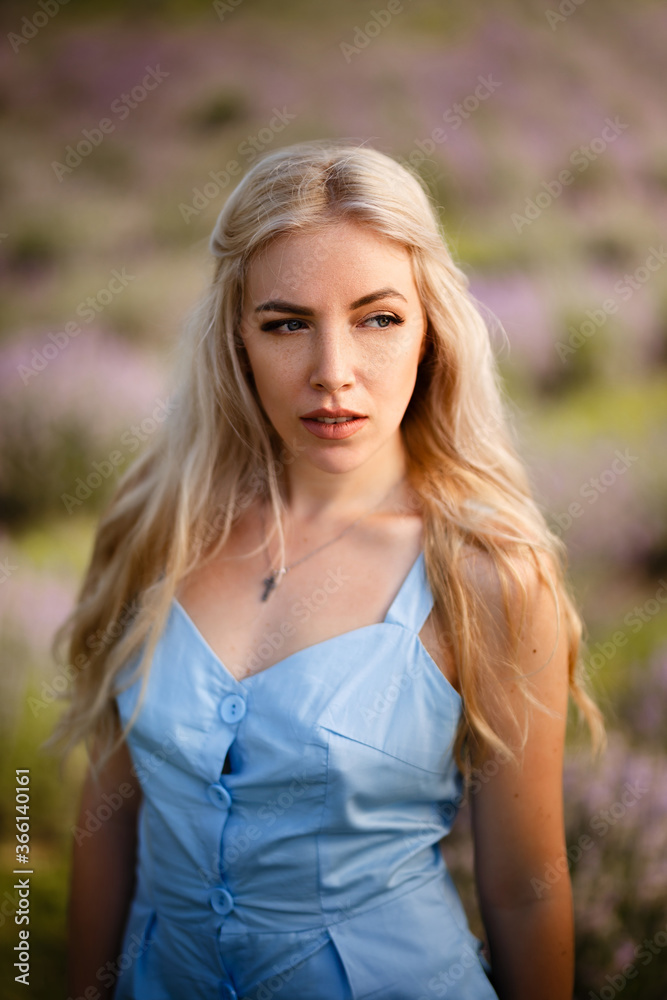 Blonde girl on a lavender field in a straw hat and blue dress.