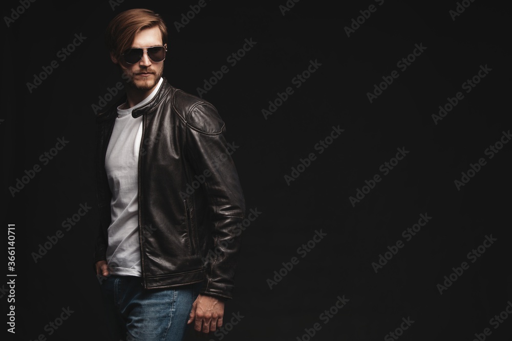 Fashion man, Handsome serious beauty male model portrait wear sunglasses and leather jacket, young guy over black background Fashion man, Handsome serious beauty male model portrait wear sunglasses and leather jacket, young guy over black background