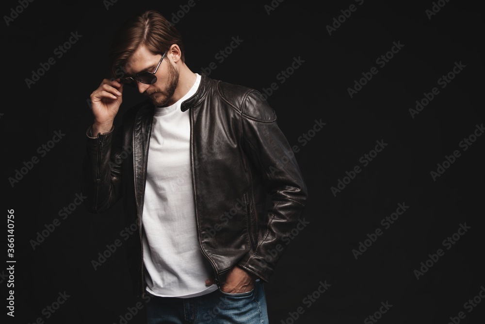Fashion man, Handsome serious beauty male model portrait wear sunglasses and leather jacket, young guy over black background Fashion man, Handsome serious beauty male model portrait wear sunglasses and leather jacket, young guy over black background