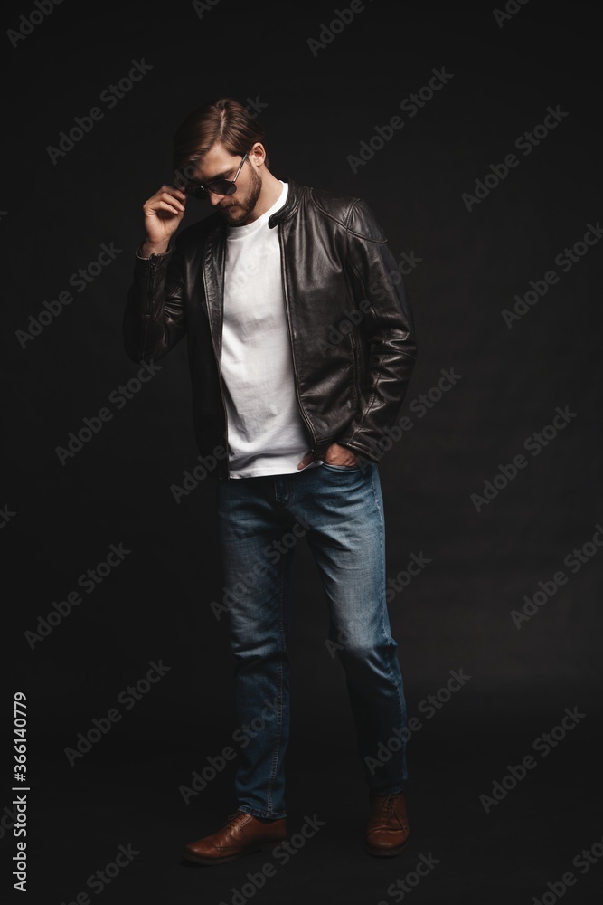 Fashion man, Handsome serious beauty male model portrait wear sunglasses and leather jacket, young guy over black background Fashion man, Handsome serious beauty male model portrait wear sunglasses and leather jacket, young guy over black background