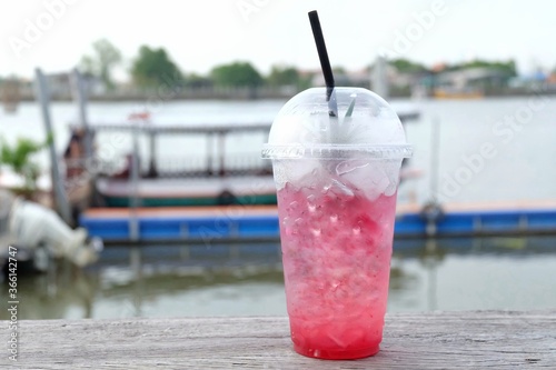 A bottle of sweet iced red cocktail on old wooden balconyin outdoor space,blurred a boat in a river and water view photo