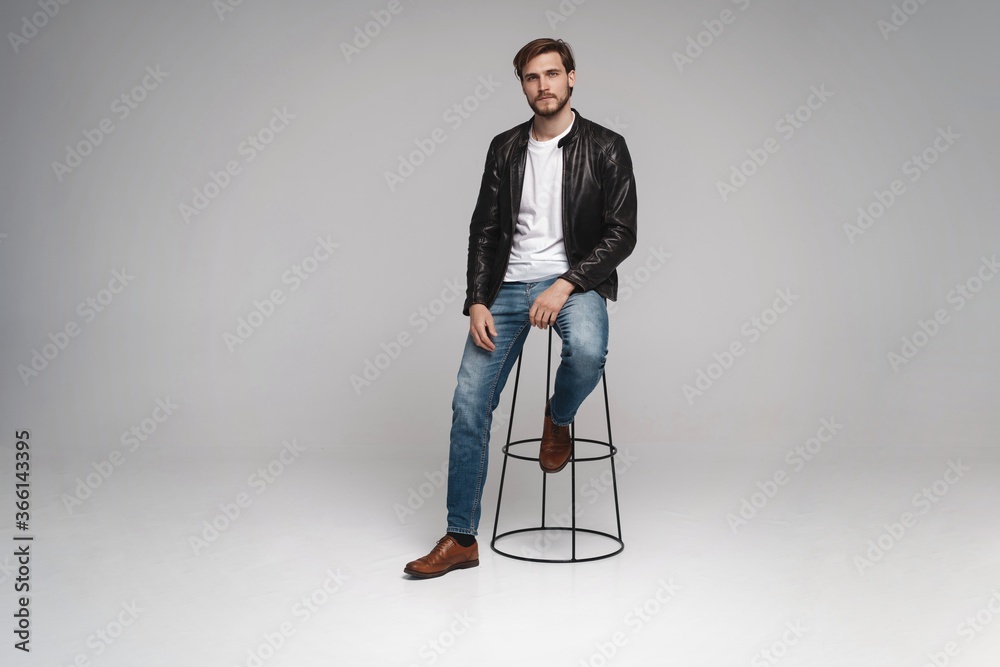 Fashion man, Handsome serious beauty male model portrait wear leather jacket, sitting on chair over white background Fashion man, Handsome serious beauty male model portrait wear leather jacket, sitting on chair over white background