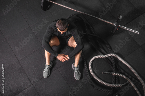Relaxing after training. Top view of bearded young man looking away while sitting on exercise mat at gym.