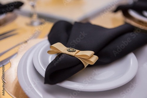 Um guardanapo de tecido preto com enfeite dourado, dentro do prato. photo