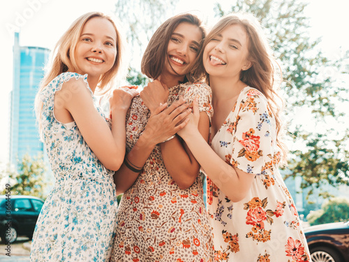 Three young beautiful smiling hipster girls in trendy summer sundress.Sexy carefree women posing on the street background. Positive models having fun and hugging.Walking after shopping