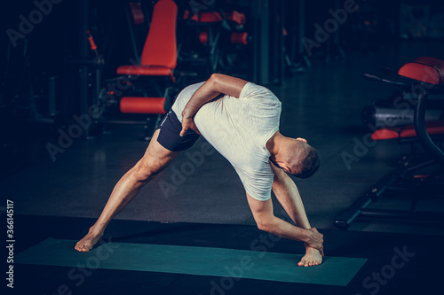 Sporty young man practicing yoga, doing stretching exercise, extended triangle pose, utthita trikonasana asana for flexible spine and relieving stress at gym.