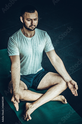 Young athletic man doing a yoga pose on a mat on a wood floor with natural light and textured wall