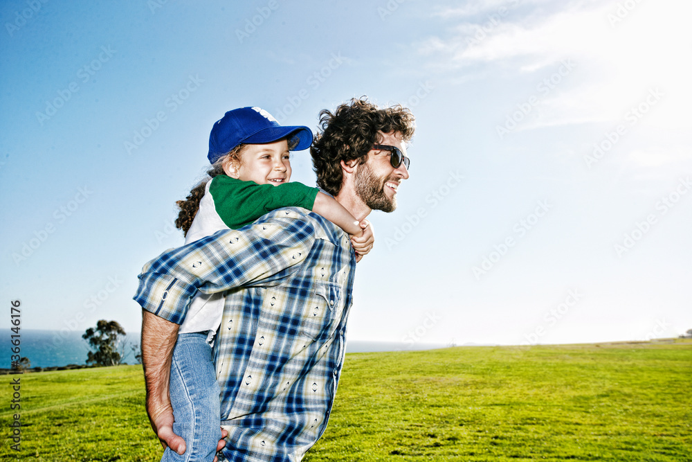Father carrying daughter piggyback in grassy field Father carrying daughter piggyback in grassy field