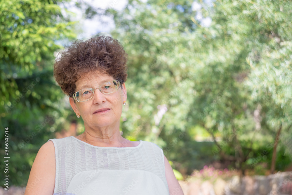 An elderly woman in glasses sits in nature and looks at the camera. The concept of old age, wisdom and joy. An elderly woman in glasses sits in nature and looks at the camera. The concept of old age, wisdom and joy.