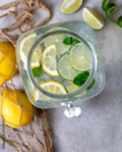 Lemonade in a glass jug with a non-standard view from above. Lemons in a string bag. Zero waste. Refreshing summer lemonade with lime lemon and mint. Spiral and lime wedges
