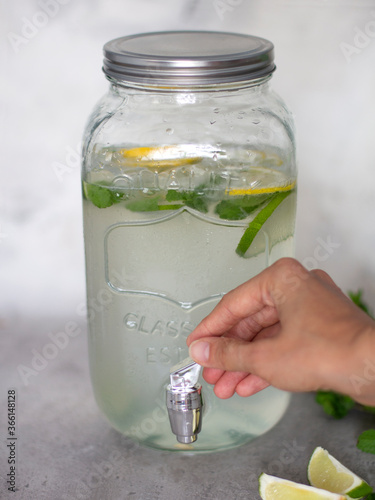 Lemonade in a glass jar with . Limonadnyj with a tap which opens the woman's hand. Refreshing summer lemonade with lime lemon and mint