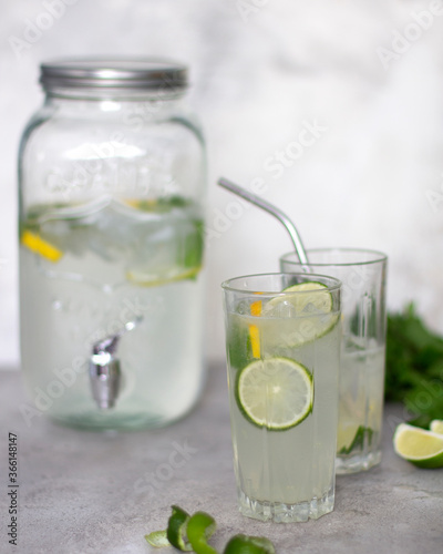 Lemonade in a glass jar with a lid and two glasses. Summer set with lemonade. Refreshing summer lemonade with lime lemon and mint in the background. Spiral and lime slices. Copy space
