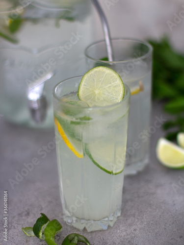 Lemonade in a glass with a slice of lime. Summer set with lemonade. Refreshing summer lemonade with lime lemon and mint in the background. Spiral and lime wedges
