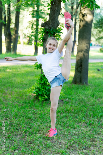 Girl child does a gymnastic exercise on the grass in the park