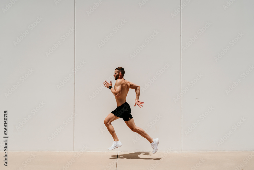 Barechested male athlete running along a wall Barechested male athlete running along a wall