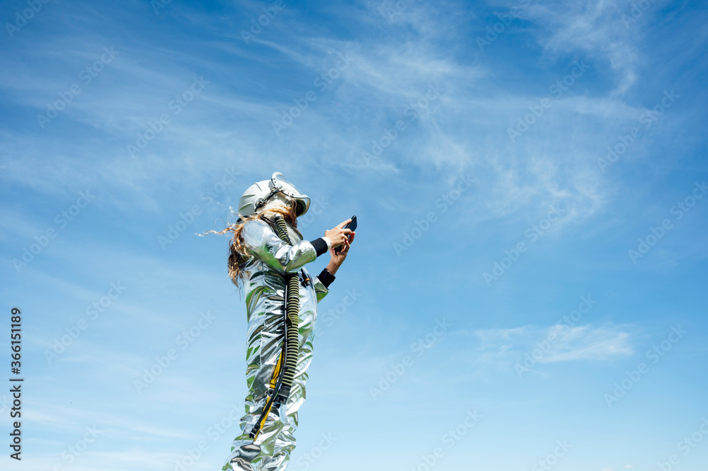 Low angle view of girl in space suit using smart phone while standing against blue sky Low angle view of girl in space suit using smart phone while standing against blue sky