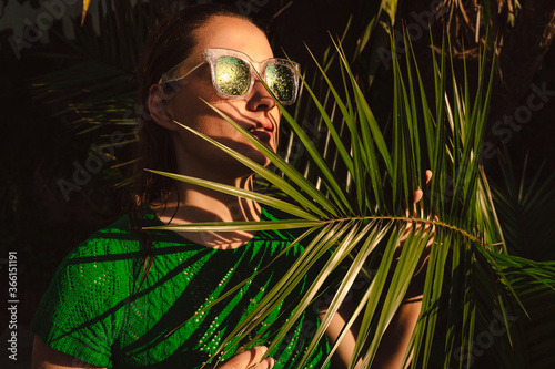 Woman with sunglasses hiding behing palm leaves photo