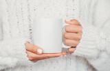 White mug mockup. Girl is holding white 11 oz ceramic cup in hands, wears cozy knitted sweater. Front view, copy space