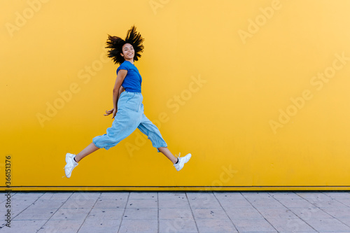 Pretty woman jumping for joy in front of yellow wall