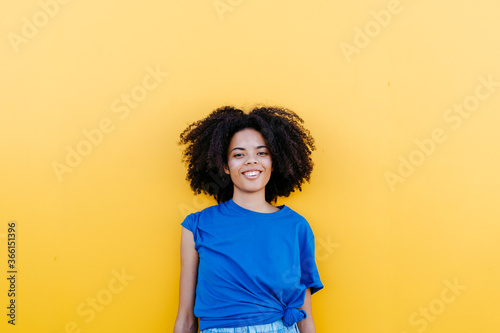 Pretty woman standing in front of yellow wall, smiling happily