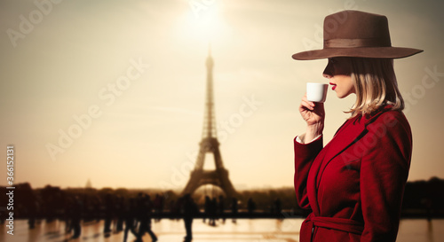girl in red coat drink a coffee wit hEiffel tower on backgorund