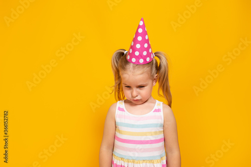 Unhappy blonde caucasian girl with sad or boring face on yellow studio background. Bad birthday party.