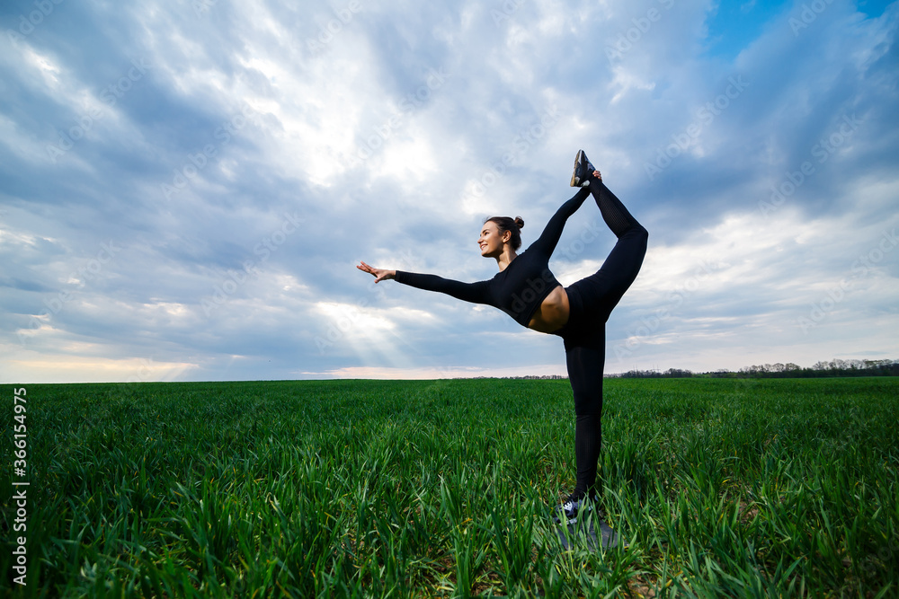 beautiful girl gymnast on the green grass do yoga. A beautiful young woman on a green lawn performs acrobatic elements. flexible gymnast in black does a handstand in split beautiful girl gymnast on the green grass do yoga. A beautiful young woman on a green lawn performs acrobatic elements. flexible gymnast in black does a handstand in split