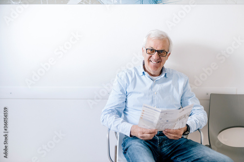 Senior man sitting in waiting room of medical practice, reading leaflet