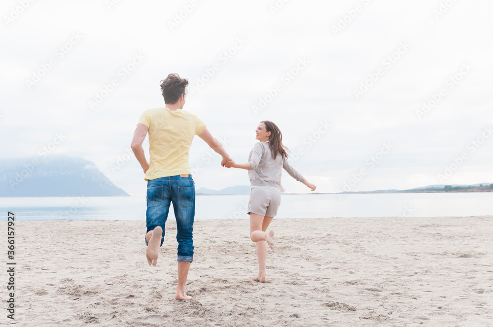 Happy couple running hand in hand on the beach, Sardinia, Italy Happy couple running hand in hand on the beach, Sardinia, Italy