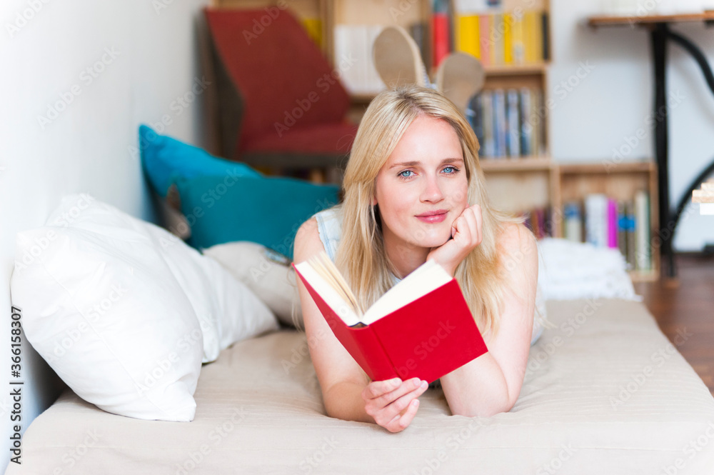 Portrait of smiling blond woman lying on couch with a book Portrait of smiling blond woman lying on couch with a book