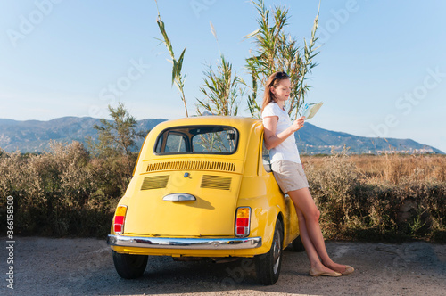 Woman leaning at yellow vinage car looking at map, Sardinia, Italy