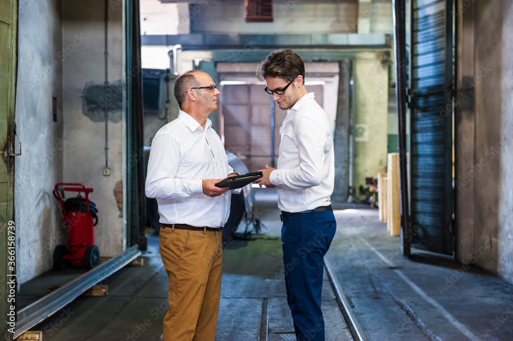 Two businessmen having a meeting in a factory hall Two businessmen having a meeting in a factory hall