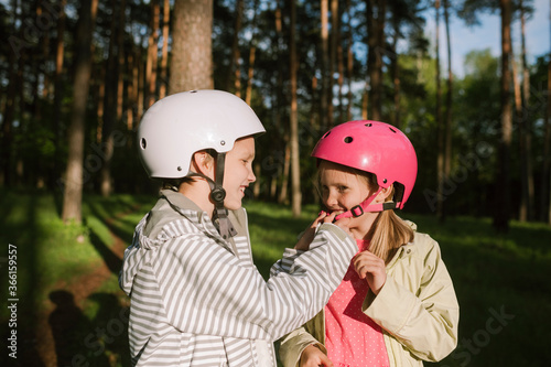 Happy boy fastening cycling helmet for girl in forest