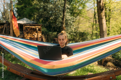 Young woman studying on laptop while sitting in hammock against trees