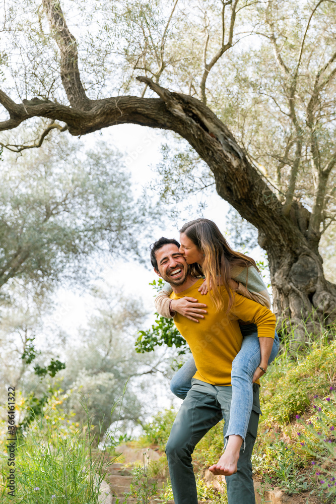 Cheerful man piggybacking romantic girlfriend while standing against trees at countryside