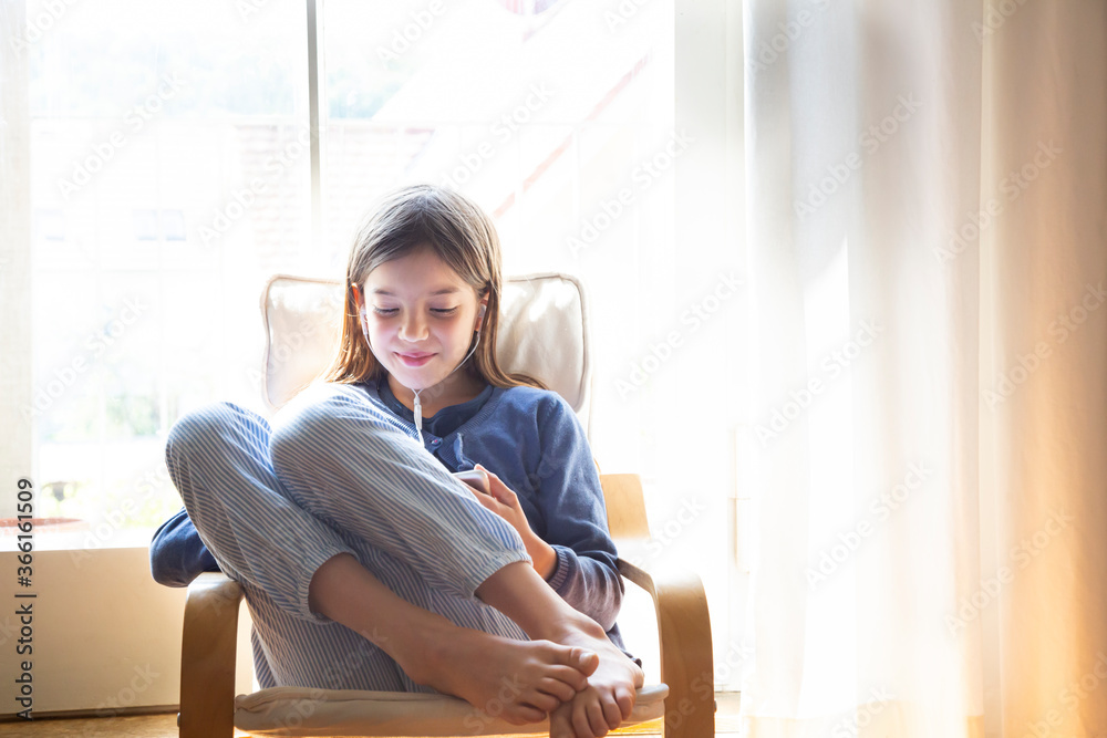 Girl watching video while sitting on armchair against window at home Girl watching video while sitting on armchair against window at home