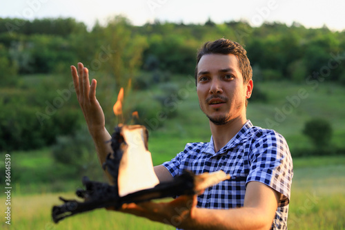 White Caucasian young man or adult guy reading a burning book on blurred forest background. Emotion of expression photo