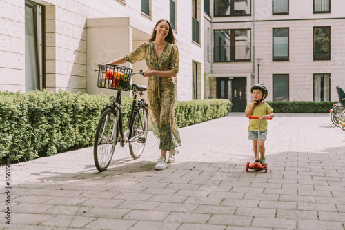 Smiling mother with bicycle and son with scooter in the city photo