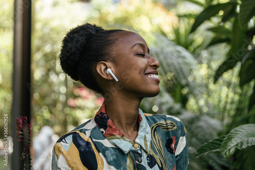 Happy young woman with eyes closed listening music with earphones in garden photo