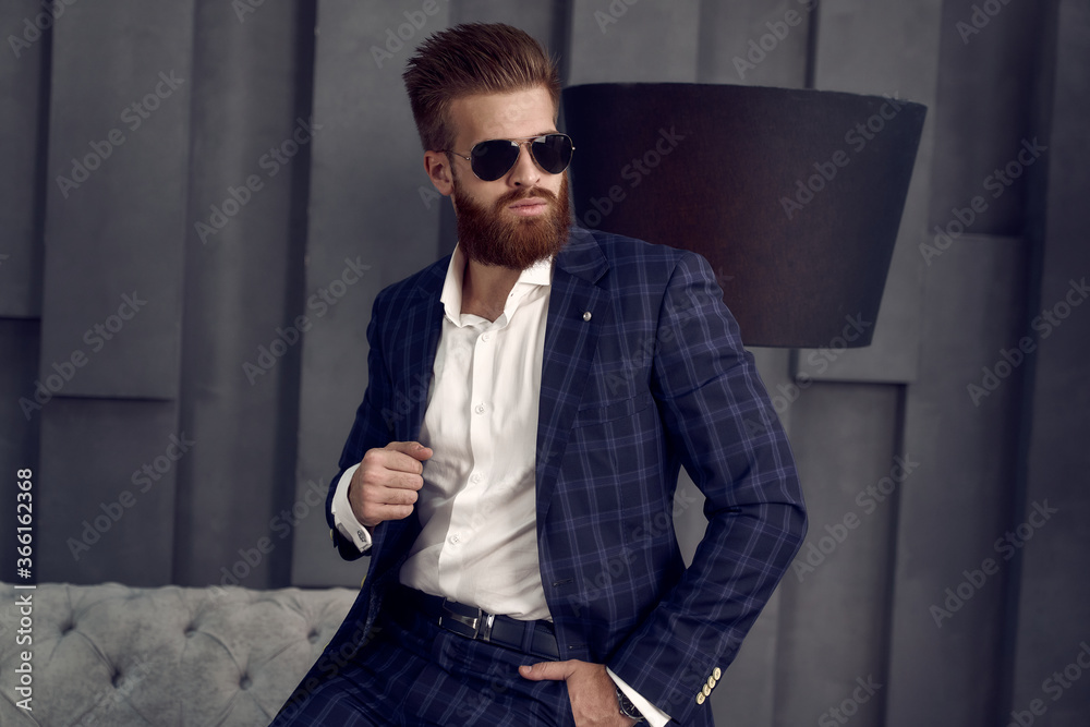 Handsome stylish man in blue suit in a cage at home sitting on sofa. Handsome stylish man in blue suit in a cage at home sitting on sofa.