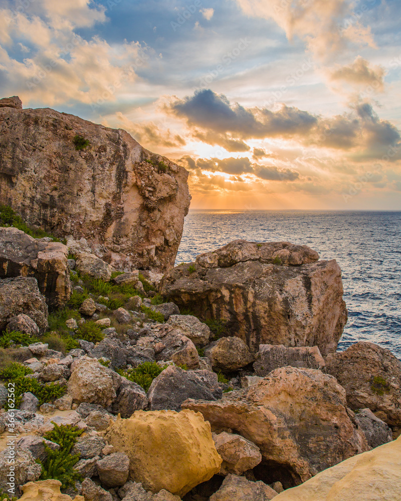 Cloud-covered sunset fills the background of a rocky Maltese landscape
