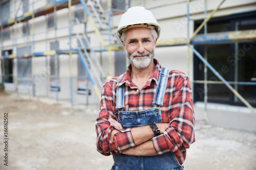 Smiling construction worker with crossed arms at construction site